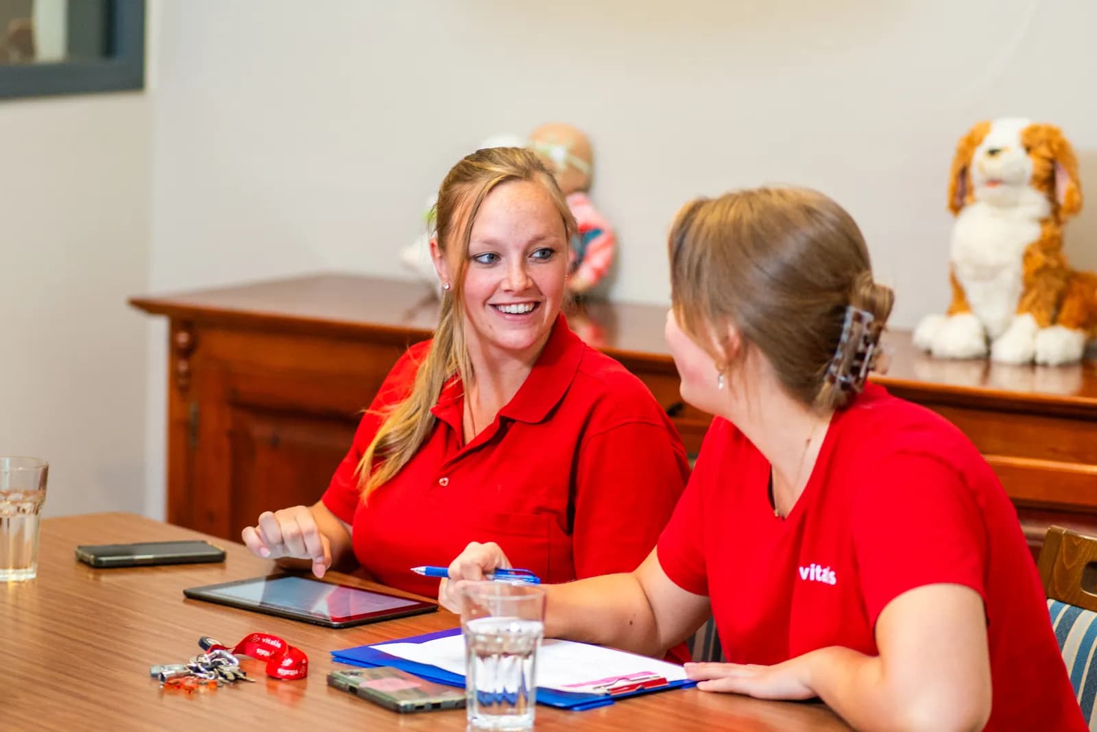 Twee zorgmedewerkers zitten aan tafel en lachen naar elkaar