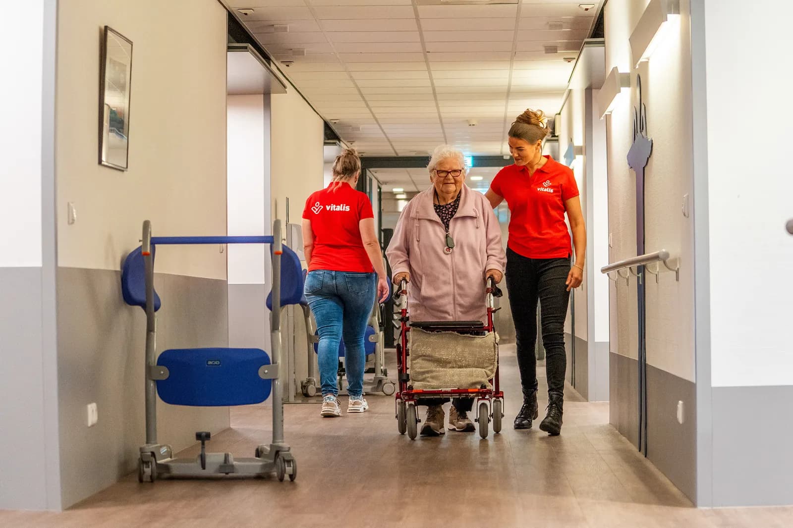 Zorgmedewerker loopt samen met oudere met rollator op de gang