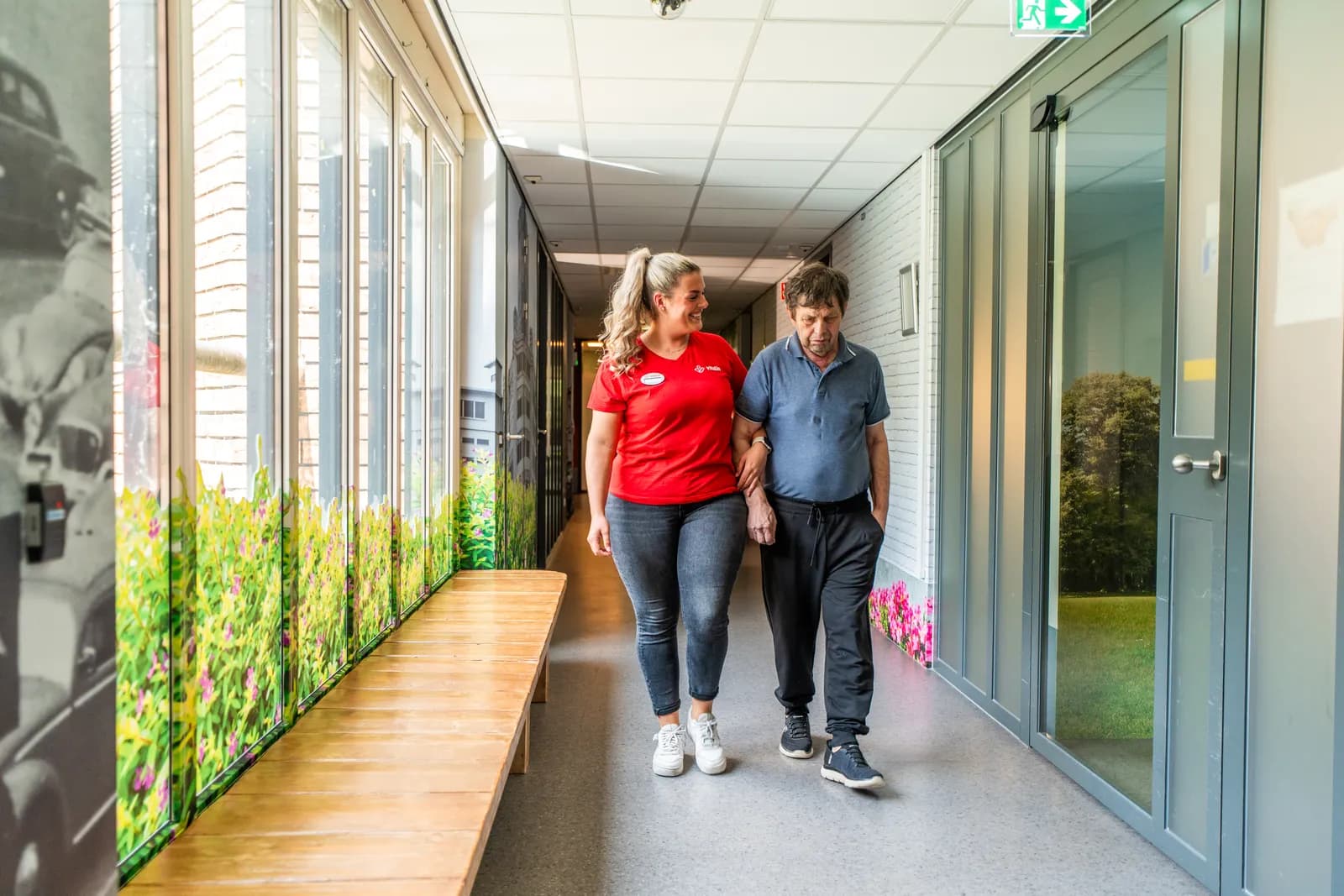 Een zorgmedewerker en een oudere lopen op de gang