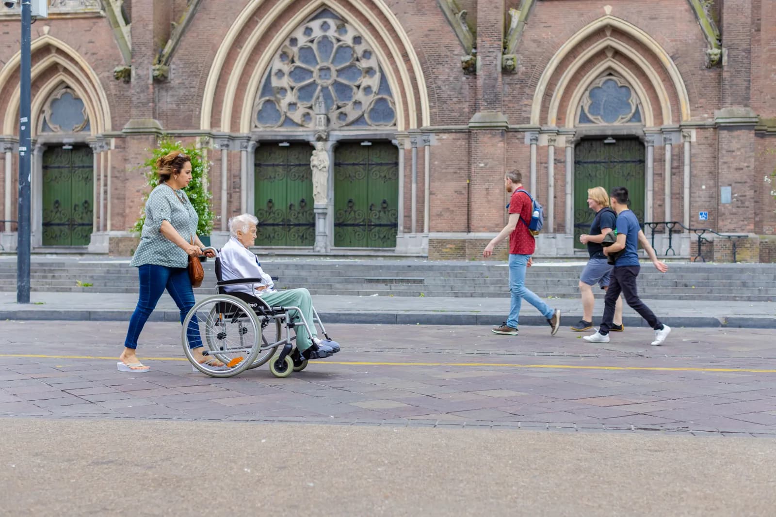 Vrijwilliger loopt samen met oudere in rolstoel voor de kerk in Eindhoven