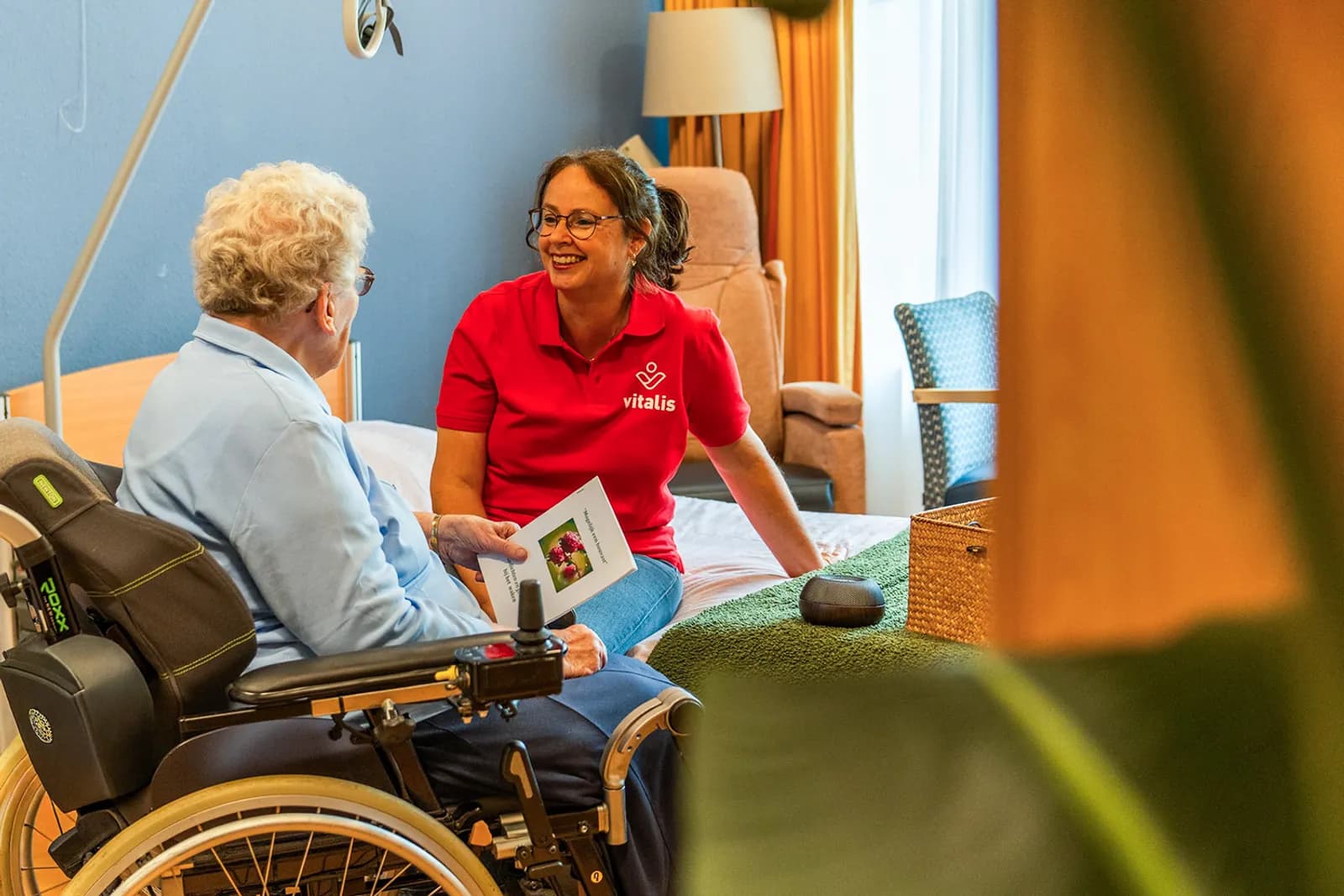 Zorgmedewerker zit op bed en lacht naar oudere