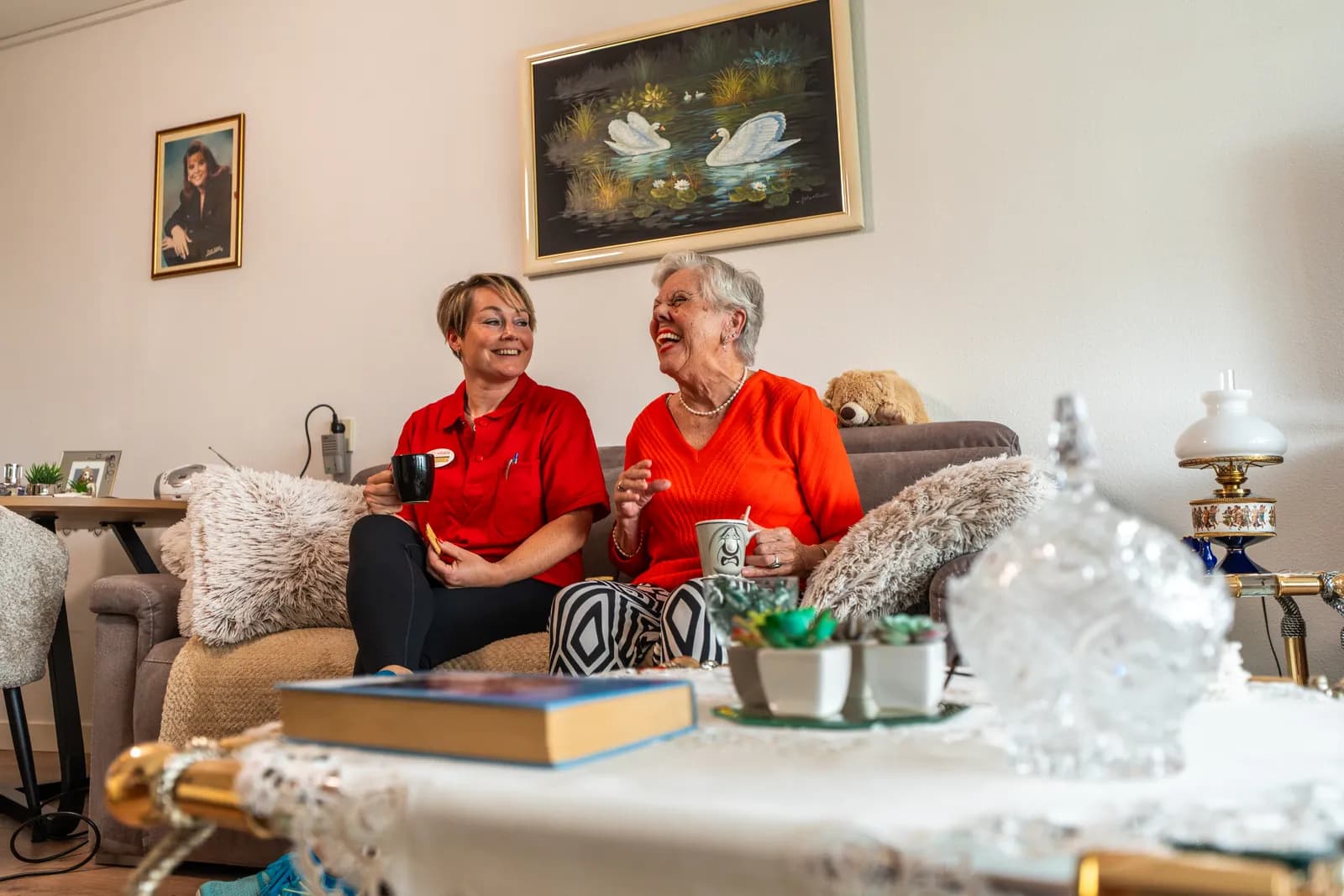 Een zorgmedewerker en een oudere drinken een kop koffie op de bank